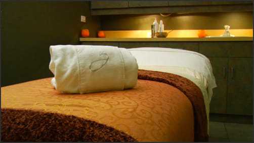 Spa treatment room with a massage table and towels. Cozy ambiance with soft lighting.