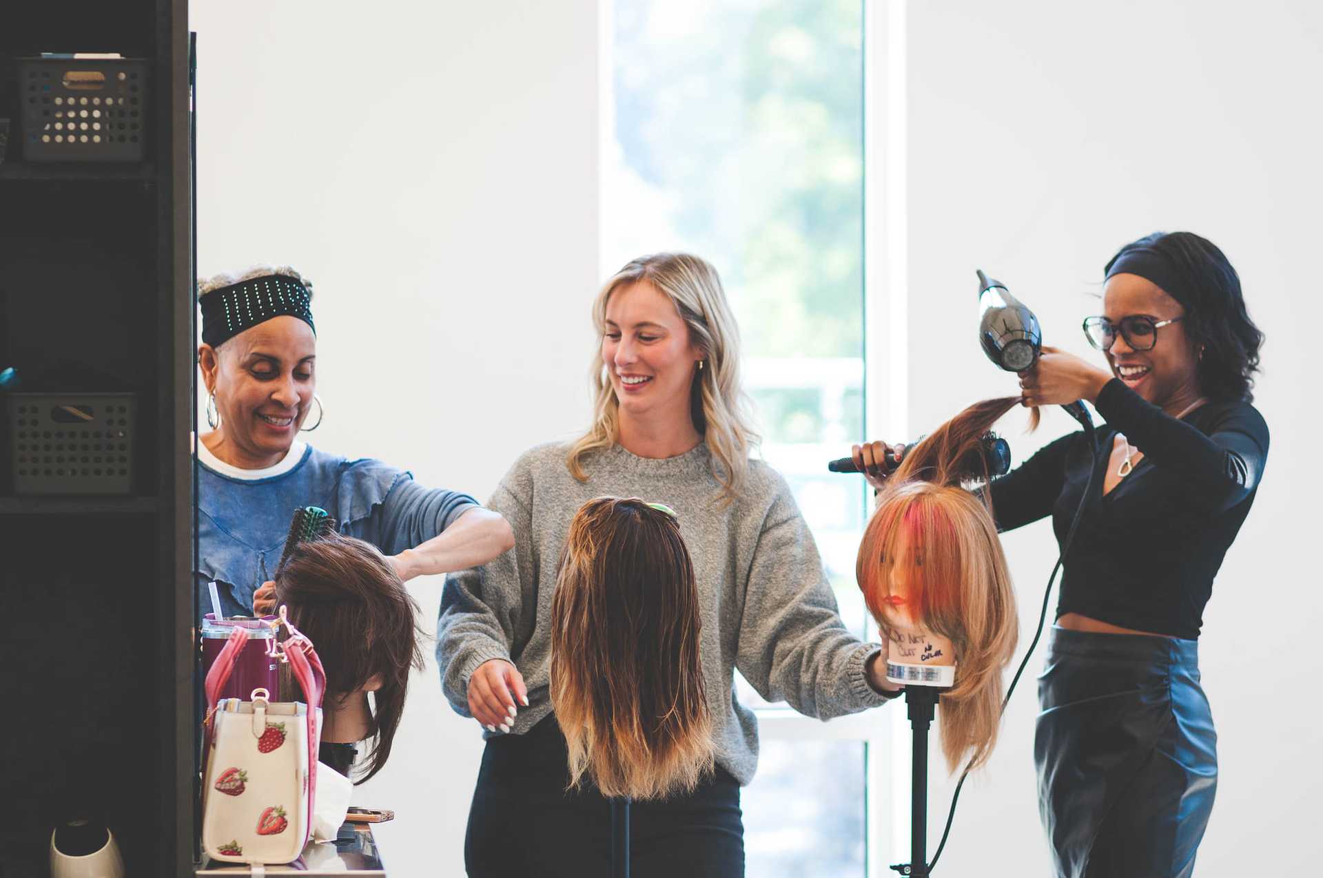 Women styling wigs on mannequin heads in a salon setting.